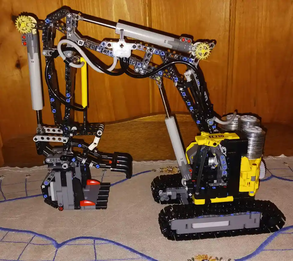 Two intricate LEGO Technic excavator models are displayed side-by-side on a patterned cloth against a wooden background. The…