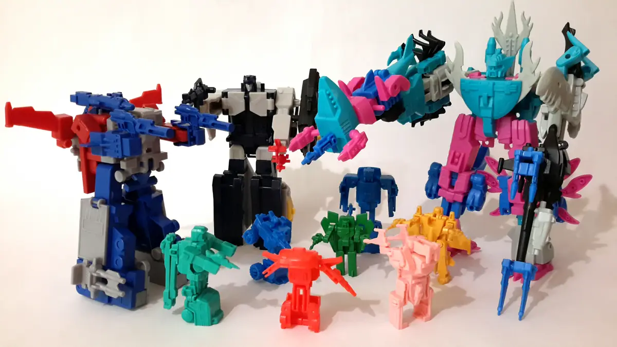 A collection of colorful toy robots, mostly Transformers, arranged on a white surface. Some are large and detailed, others…