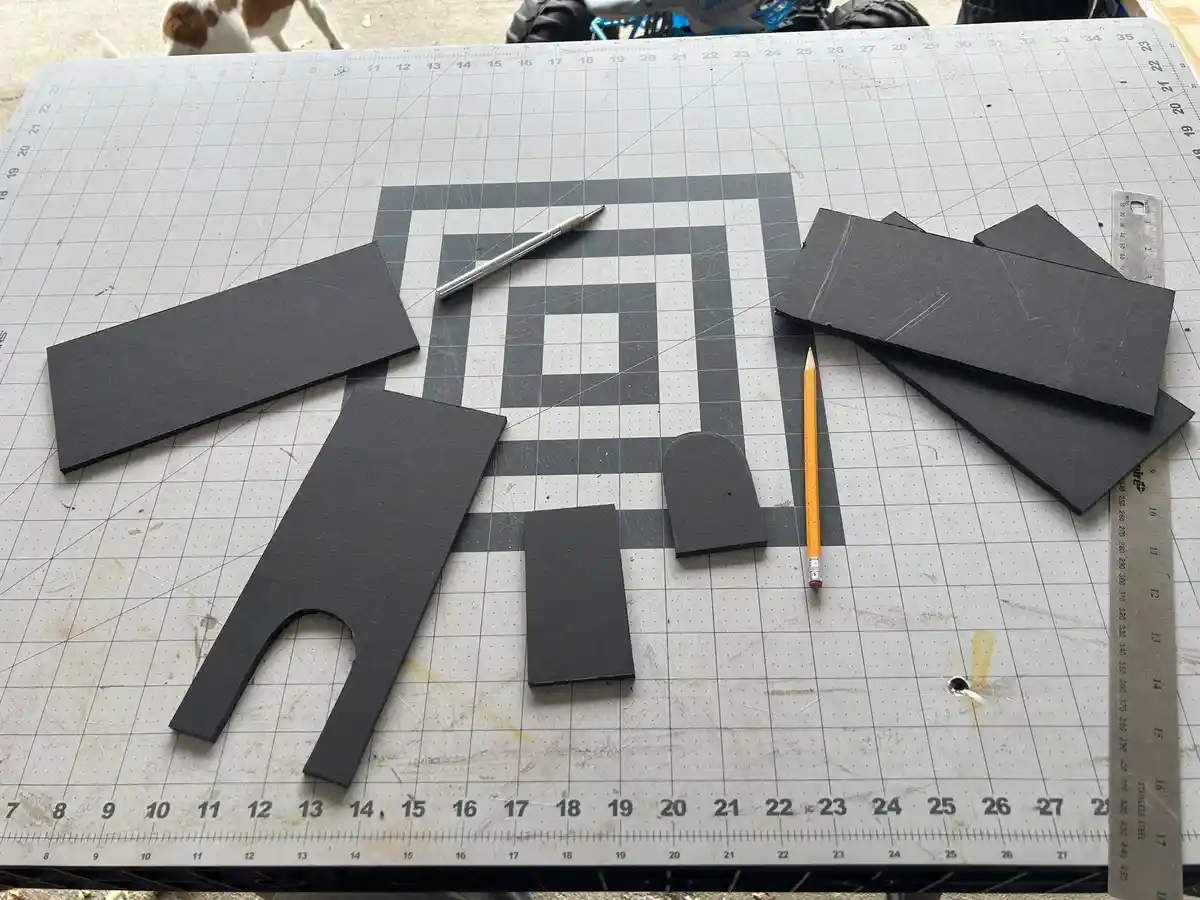 A crafting table with a grid layout holds various black foam pieces, including a large U-shaped cutout, smaller rectangles…