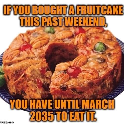 A round fruitcake with a large central hole, topped with pecans, cherries, and candied fruit, sits on a blue plate. Overlaid…