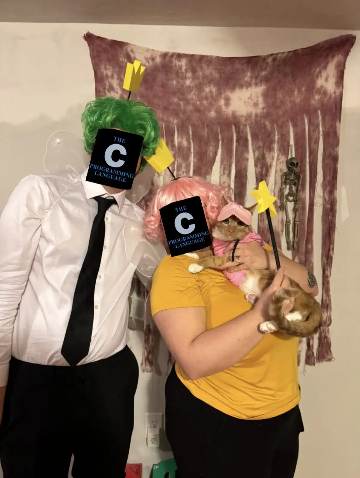 Two people dressed as fairy tale characters, one with green hair and a crown, the other with pink hair holding a cat in a…