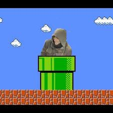 A person wearing a grey hoodie is shown sitting atop a green warp pipe from the Super Mario video game series, set against a…