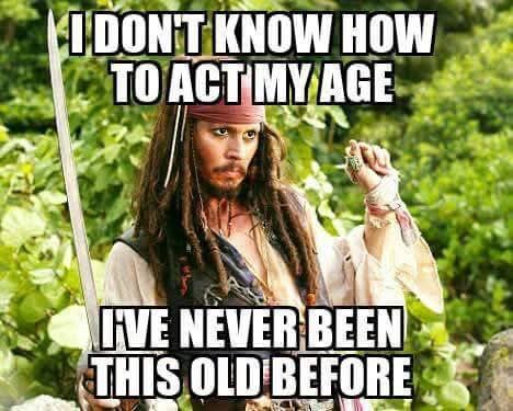 A man with long dreadlocks, a bandana, and a sword, dressed as a pirate, looks confused while holding a small object. The…