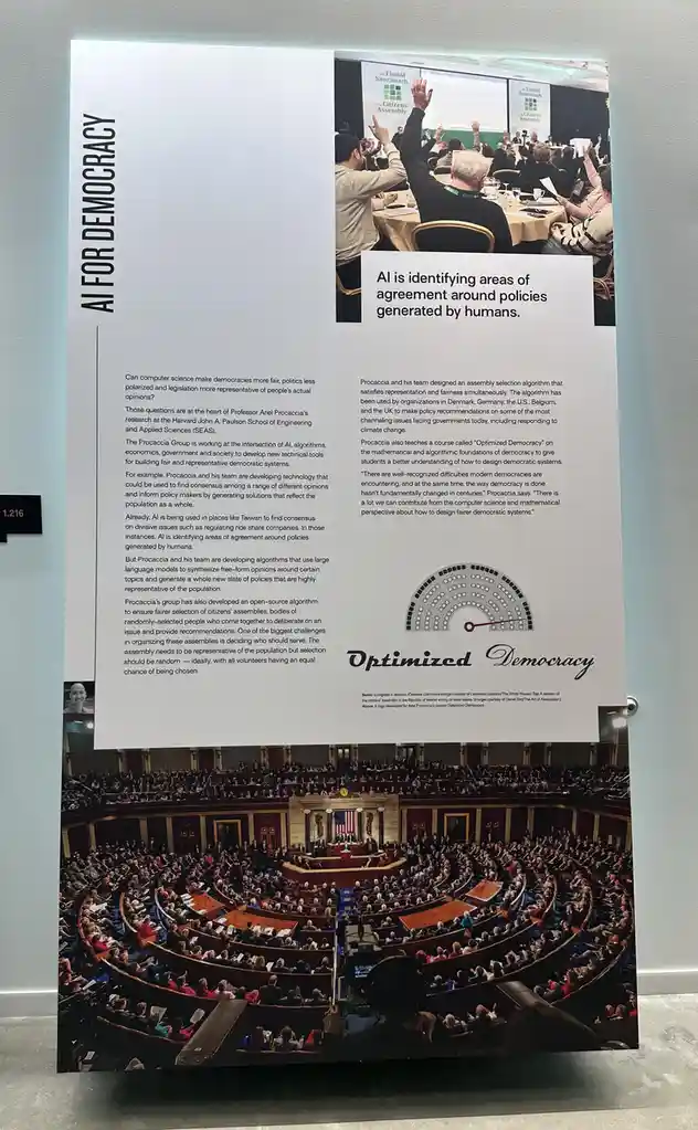 A museum exhibit panel titled 'AI FOR DEMOCRACY' displays two photos: one of a modern citizens' assembly with people raising…