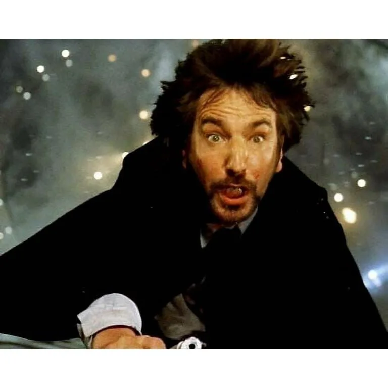 A man with wild hair and a shocked expression, wearing a dark coat over a white shirt and tie, leans forward against a…