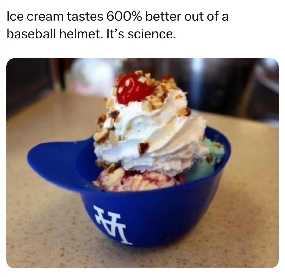 A blue baseball helmet-shaped bowl with a white 'NY' logo sits on a countertop, filled with scoops of ice cream topped with…