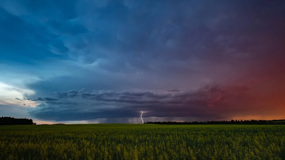 A dramatic landscape photo shows a vast green field under a stormy sky with dark clouds and a single bolt of lightning…