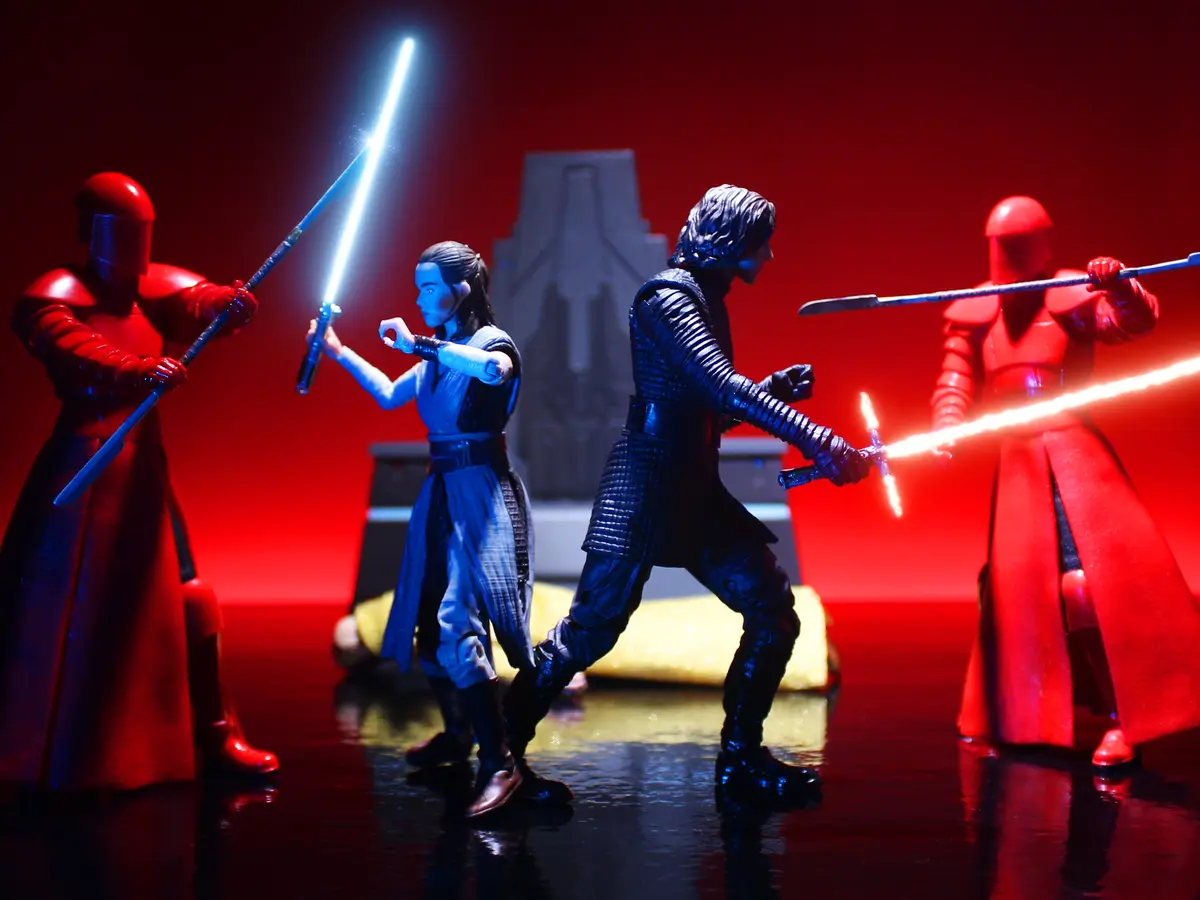A staged photo of Star Wars action figures: Rey and Kylo Ren in combat poses with lightsabers against two red-armored First…