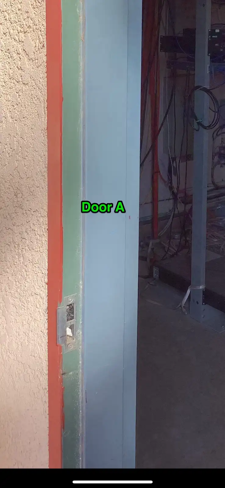 A close-up photo shows a narrow, light-blue metal door frame labeled 'Door A' in bright green text, set within a wall with…