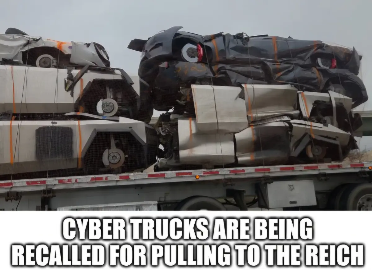 A flatbed truck carries a pile of crushed and mangled vehicles, mostly black and white, secured with orange straps and…