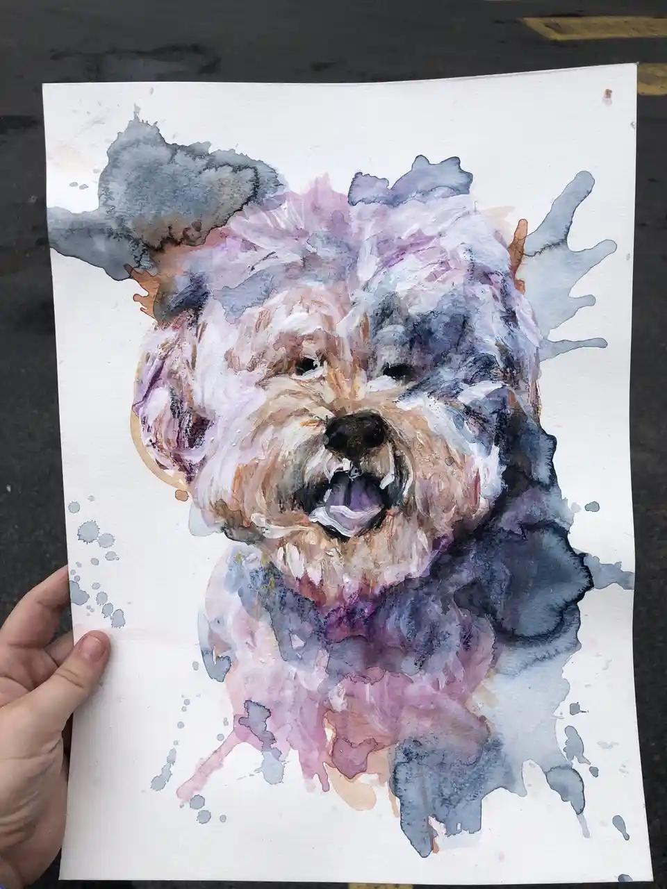 A hand holds up a watercolor painting of a fluffy dog with expressive eyes and a slightly open mouth, rendered in soft…
