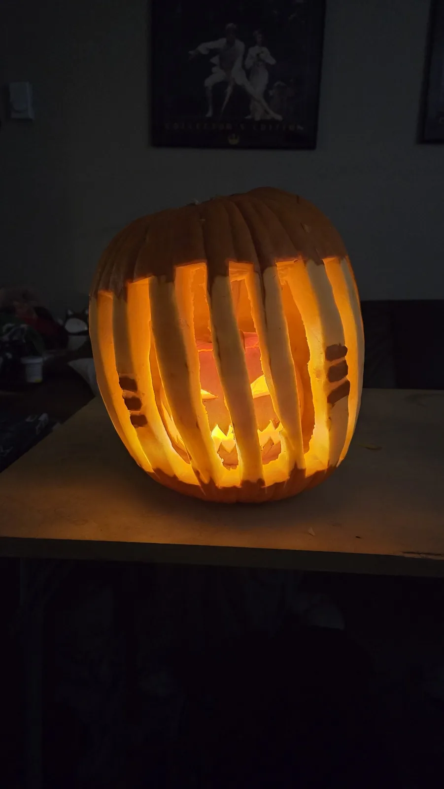 A carved Halloween pumpkin sits on a table, illuminated from within, with vertical slats carved into its sides resembling…
