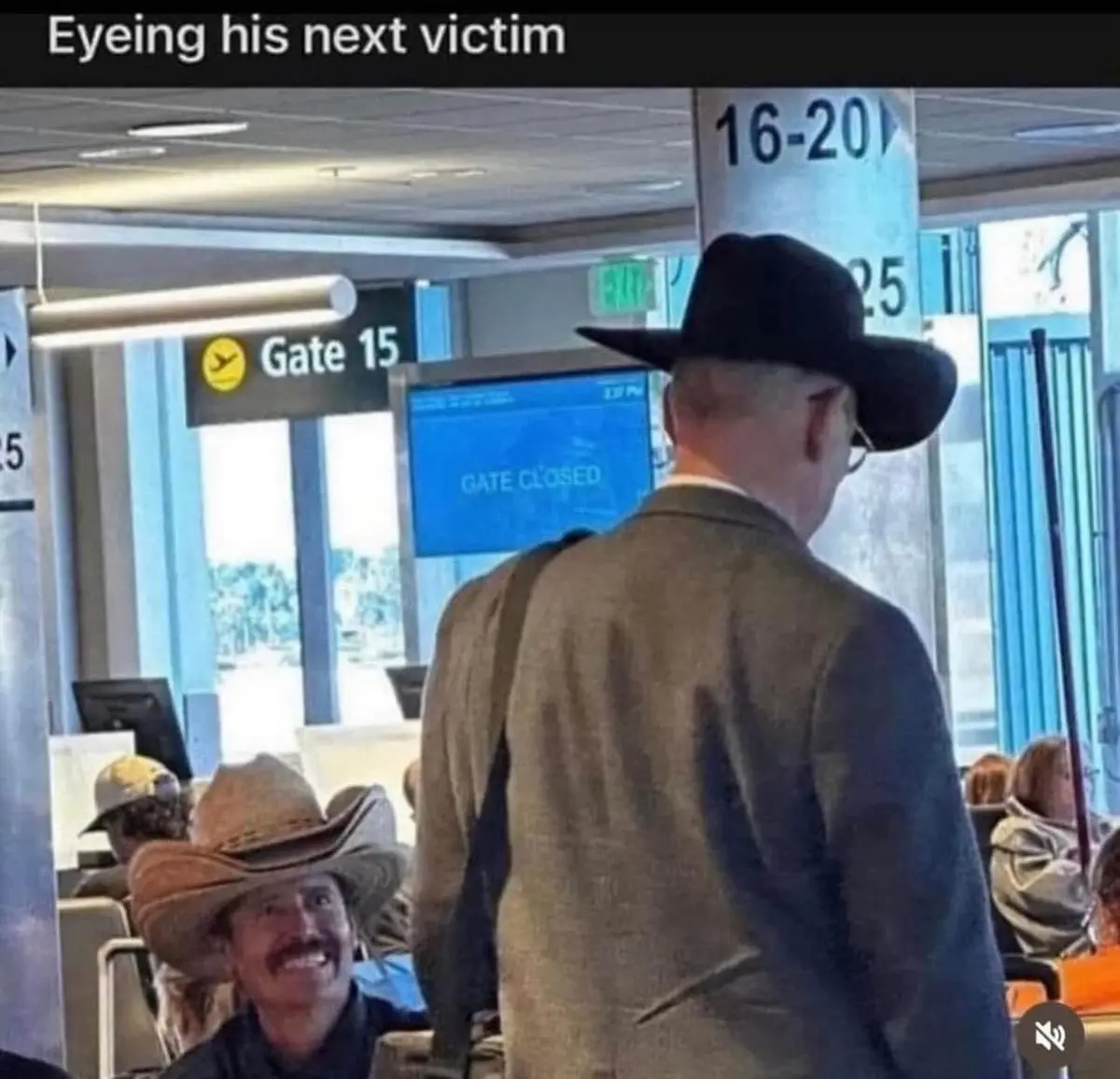 A man in a black cowboy hat stands with his back to the camera in an airport terminal, facing a gate sign that reads 'GATE…
