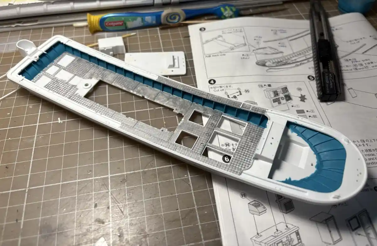 A partially assembled plastic model kit lies on a gridded cutting mat, surrounded by instruction sheets, a utility knife…