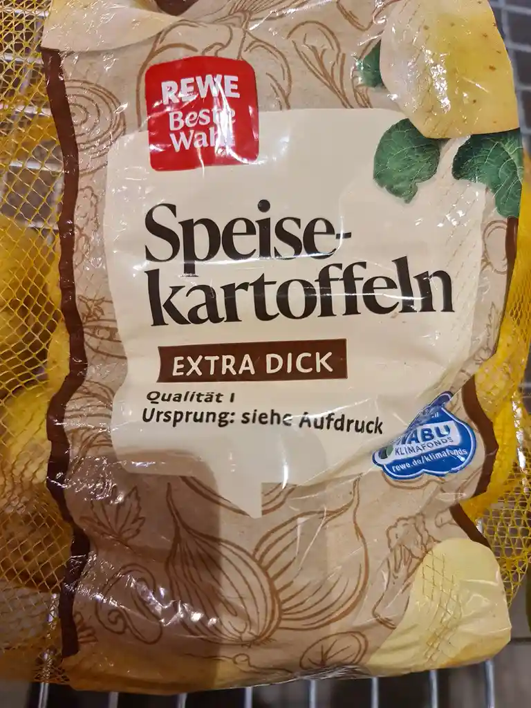 A close-up of a German grocery bag of 'Speisekartoffeln' (eating potatoes) labeled 'EXTRA DICK' (extra thick), with a 'REWE…