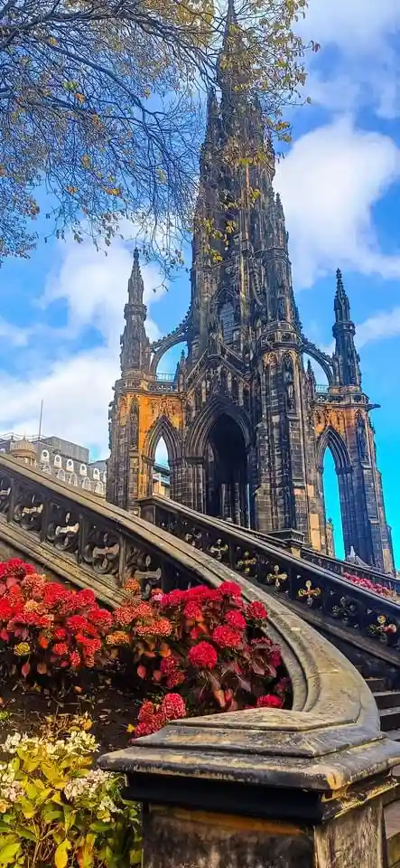 A low-angle photograph of the Scott Monument in Edinburgh, Scotland, showcasing its intricate Gothic architecture against a…