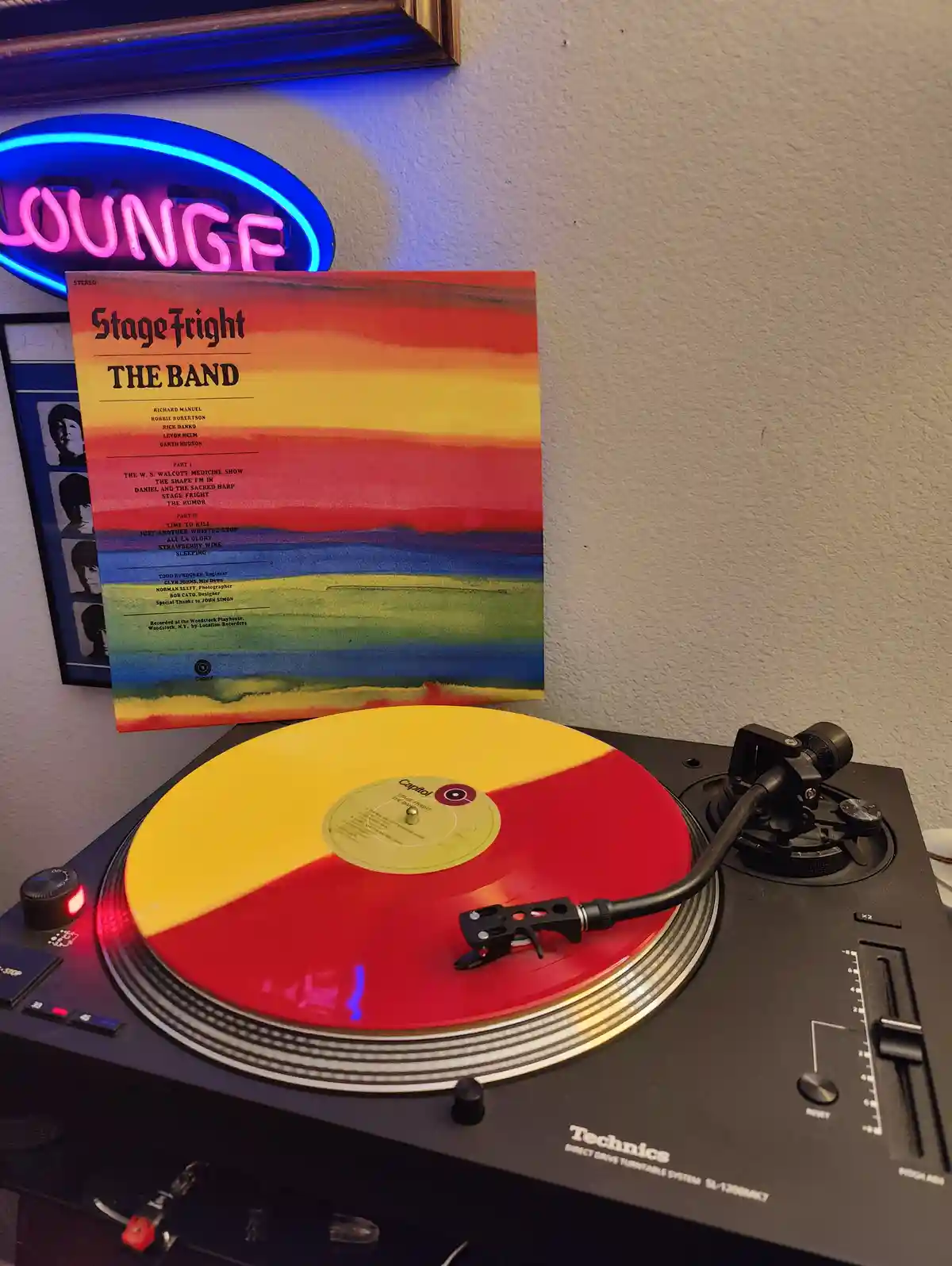 A Technics turntable plays a vinyl record with a red and yellow split design, positioned in front of the album cover for…