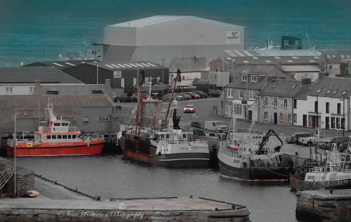 A harbor scene with several boats docked, including a red rescue boat, a large fishing vessel named 'STELLA POLARIS', and…