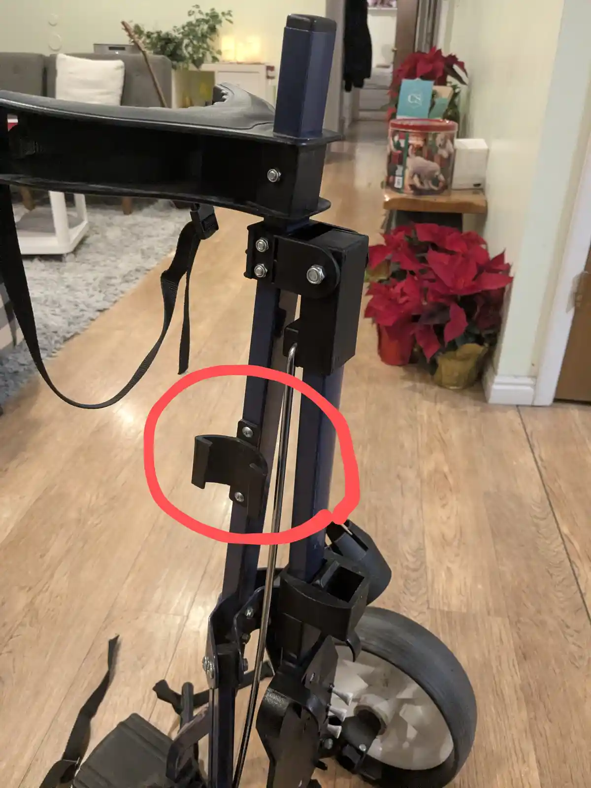 A close-up photo of a black mobility walker with a red circle highlighting a small, U-shaped metal bracket attached to its…