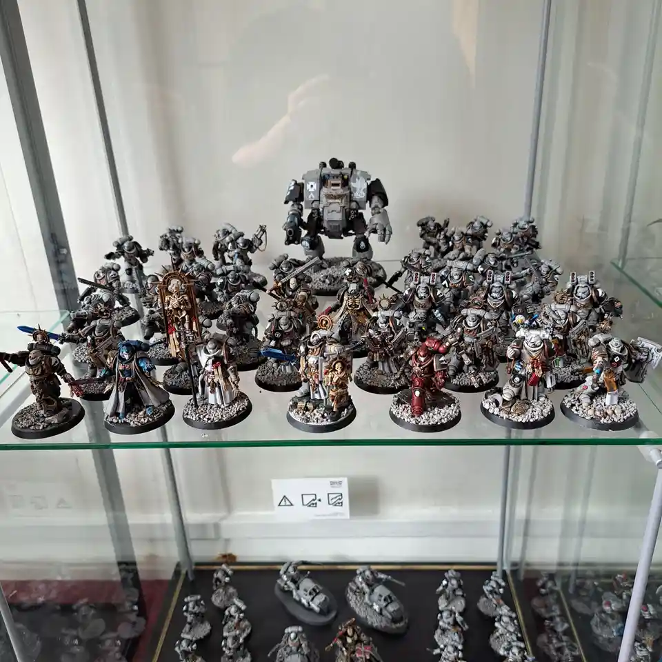 A glass display case holds dozens of intricately painted Warhammer 40,000 miniatures, including a large central robot and…