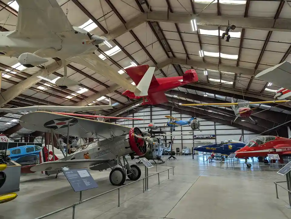 An indoor aviation museum with numerous vintage and modern aircraft displayed on the floor and suspended from the high…