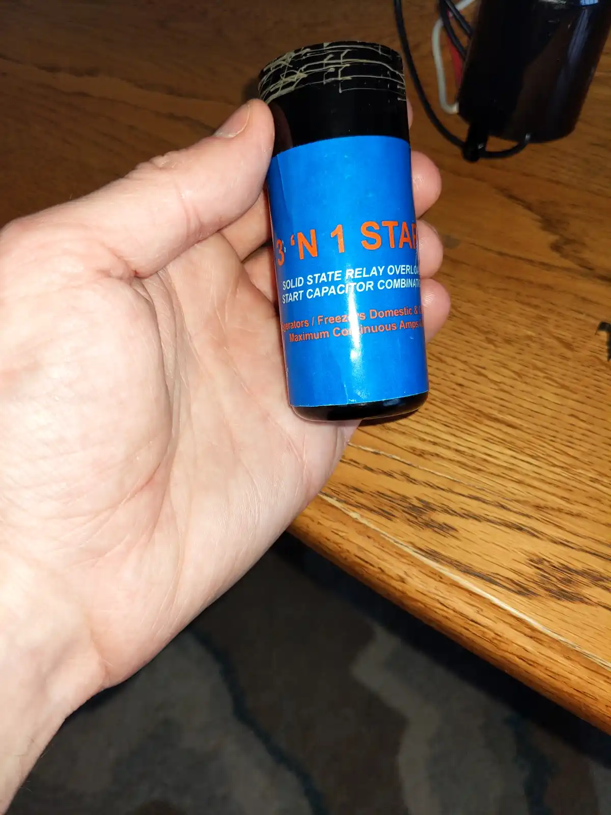A hand holds a small black cylindrical electronic component with a blue label that reads '3 'N 1 START SOLID STATE RELAY…