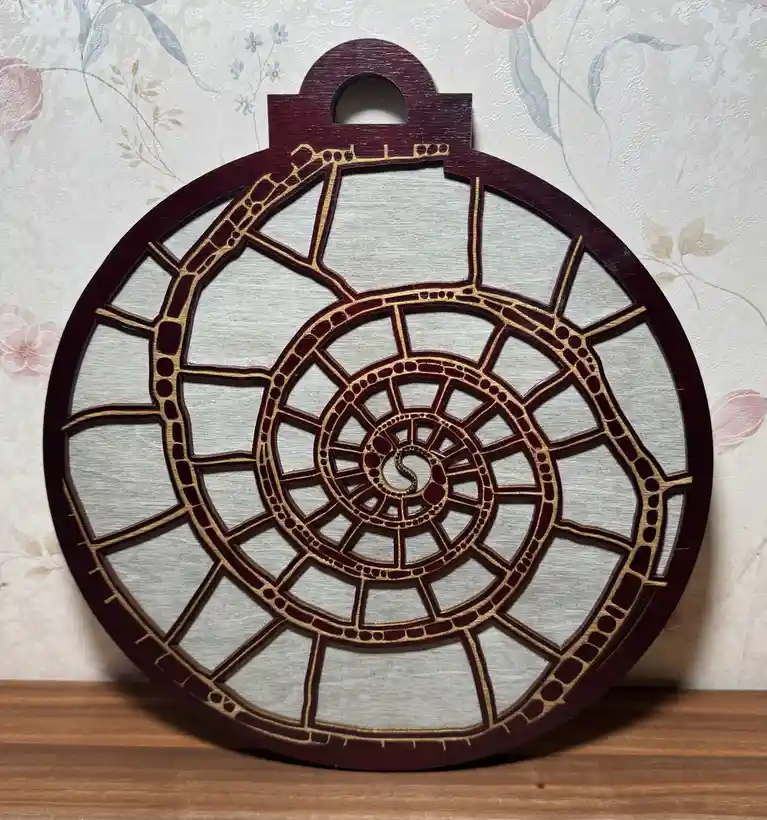 A circular wooden decorative piece with a dark red border and gold inlay, featuring a spiral design that resembles the…