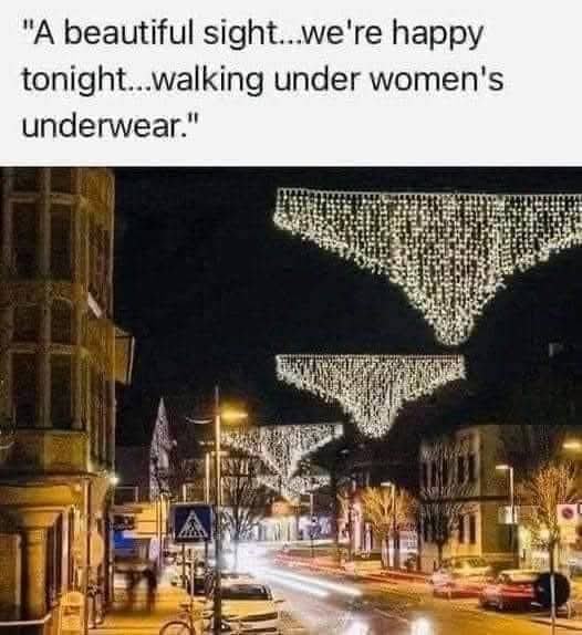A nighttime street scene with festive string lights arranged in the shape of women's underwear hanging over the road. The…