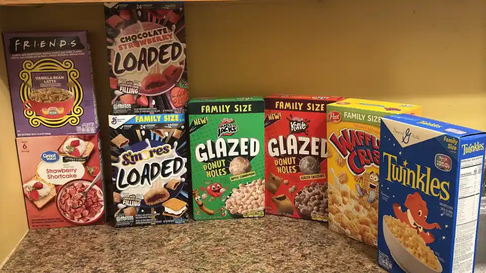 A shelf displays several large family-size cereal boxes, including Friends, Chocolate Strawberry Loaded, S'mores Loaded…