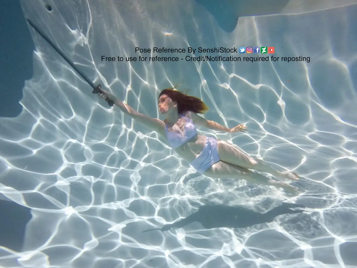 An underwater photo shows a woman in a light blue bikini holding a sword while floating in clear water, with sunlight…