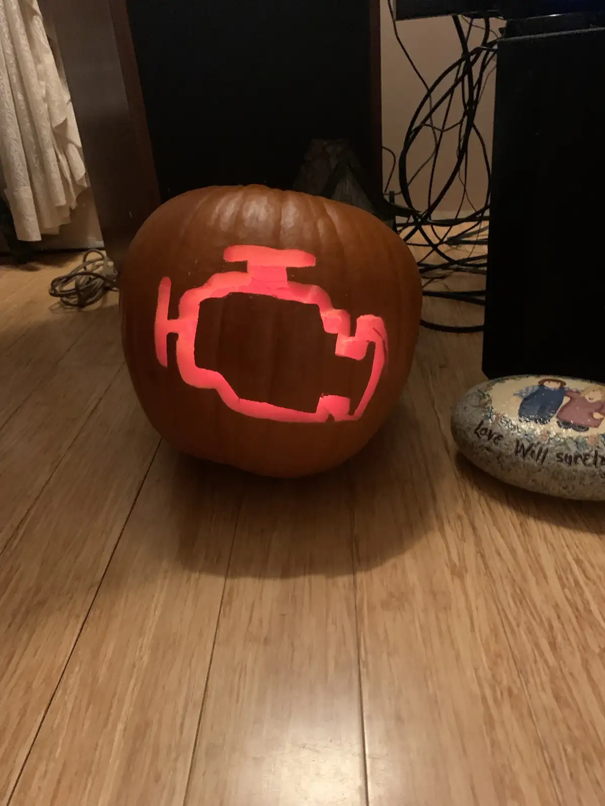 A carved pumpkin with a glowing red outline of an engine symbol on its front, sitting on a wooden floor next to a decorative…