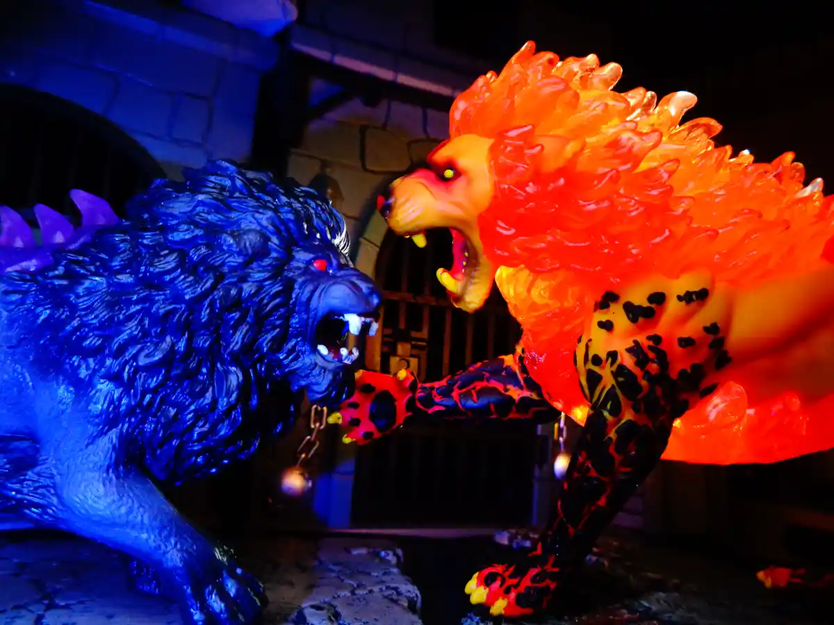 Two toy lion statues face off in a dramatic pose, one glowing fiery orange-red with black spots and the other glowing icy…