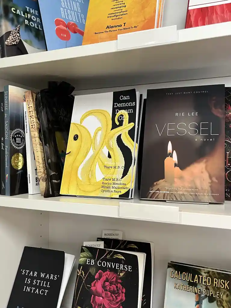 A bookshelf displays various books, including one titled 'Can Demons Dream Of..' with a yellow, stitched, cartoonish octopus…