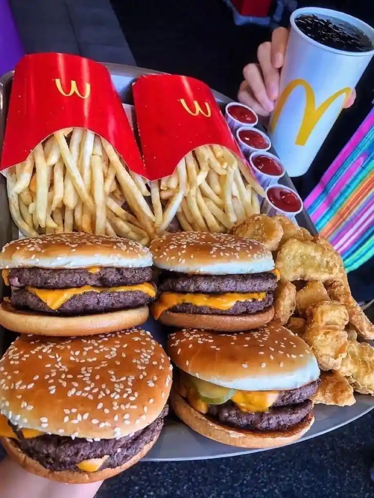 A person holds a large tray overflowing with four McDonald's burgers, two red paper containers of fries, a side of chicken…