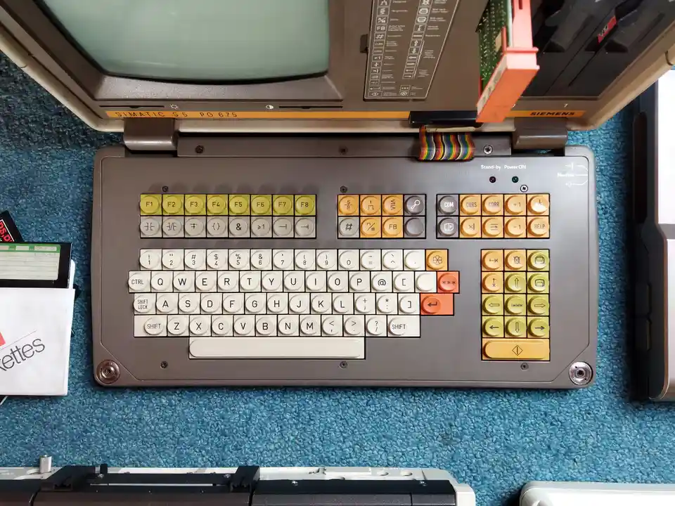 A top-down photo of a vintage Siemens SIMATIC S5 PG 675 industrial programming terminal with a built-in keyboard, featuring…