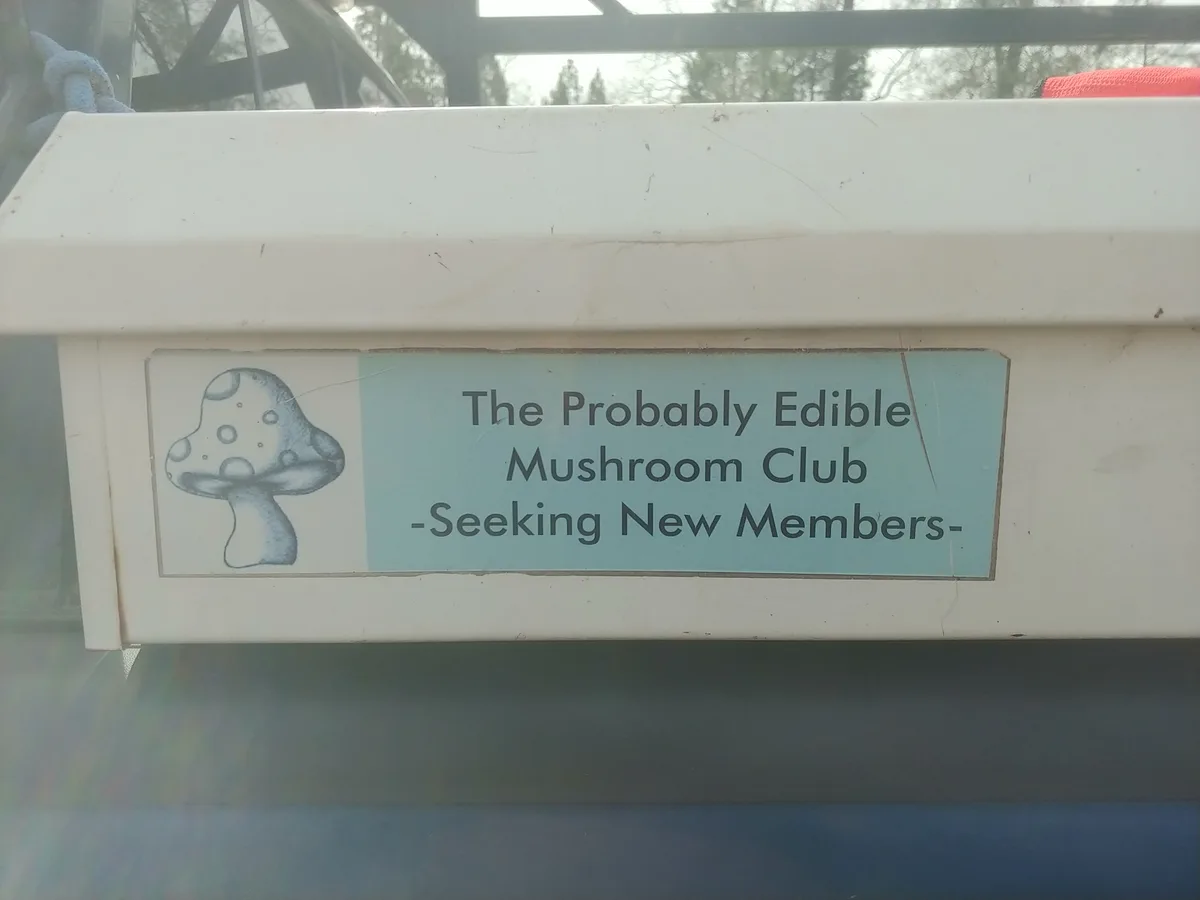 A close-up of a light blue sticker on a white plastic box, featuring a simple pencil drawing of a spotted mushroom on the…