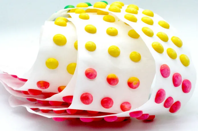 A roll of white paper with colorful candies stuck to it, showing a gradient from yellow to pink, with overlaid text reading…