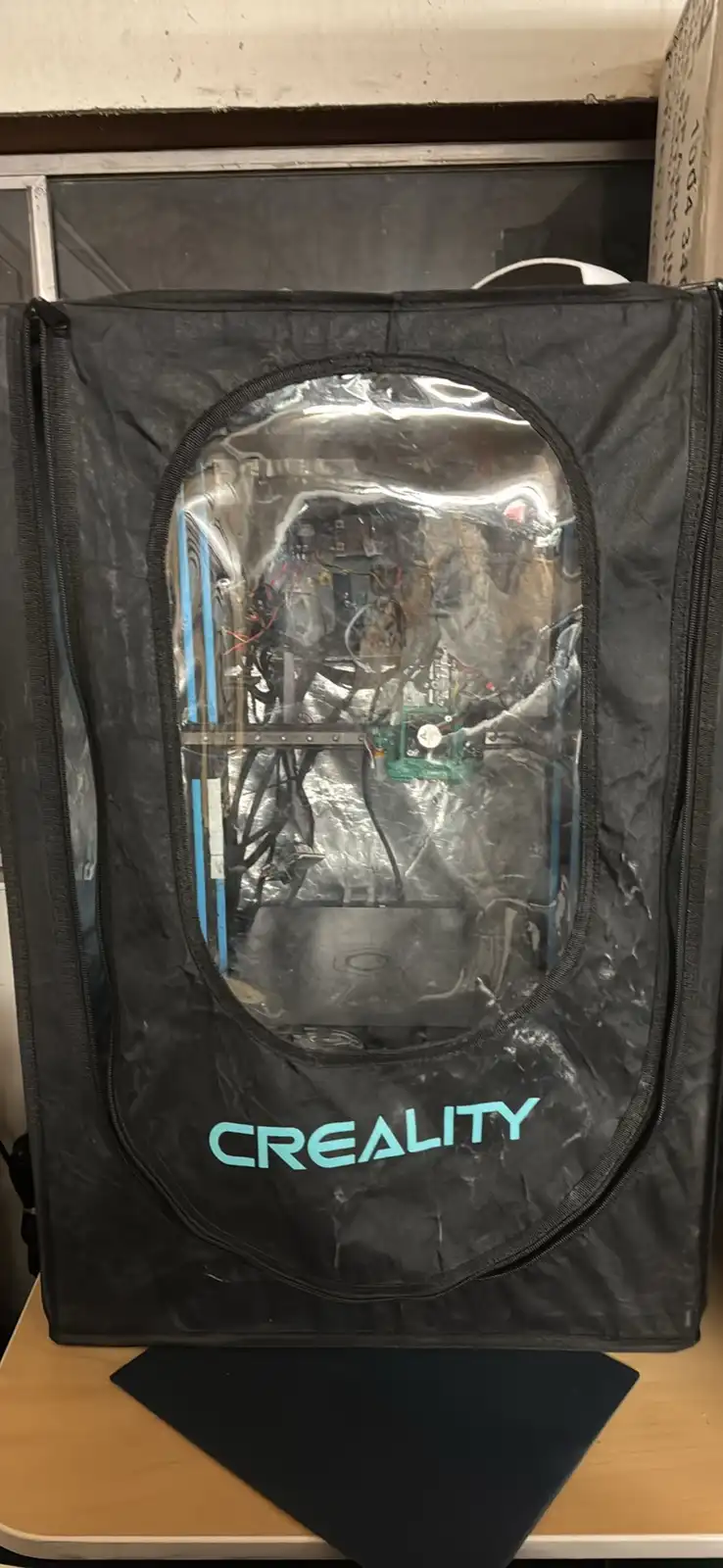 A black, zippered carrying case with a clear plastic window, branded with 'CREALITY' in teal lettering, is open to reveal a…