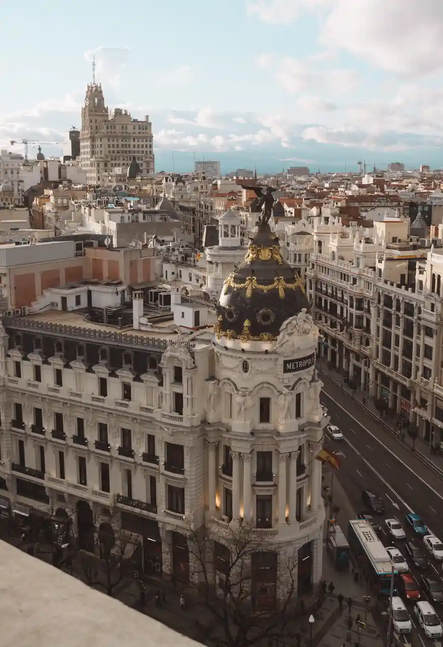 An aerial view of the ornate, white Metropolis building in Madrid, Spain, with its distinctive black and gold dome and angel…