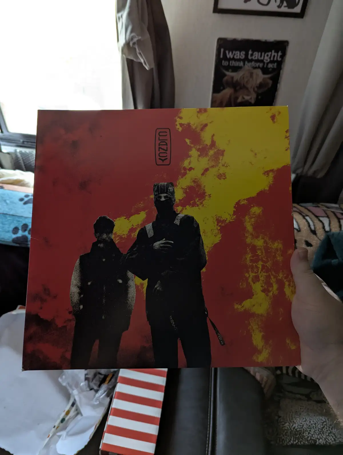 A person holds up a vinyl record album cover featuring two silhouetted figures against a red and yellow background; the text…