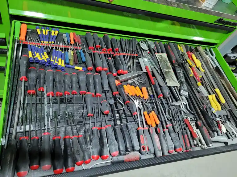 A bright green toolbox drawer is fully stocked with dozens of neatly organized screwdrivers, wrenches, and other hand tools…