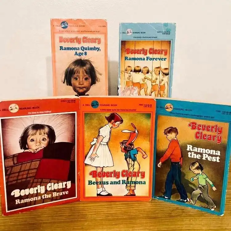 Five vintage 'Dell Yearling Book' covers of Beverly Cleary's Ramona series are arranged on a wooden surface. The books…