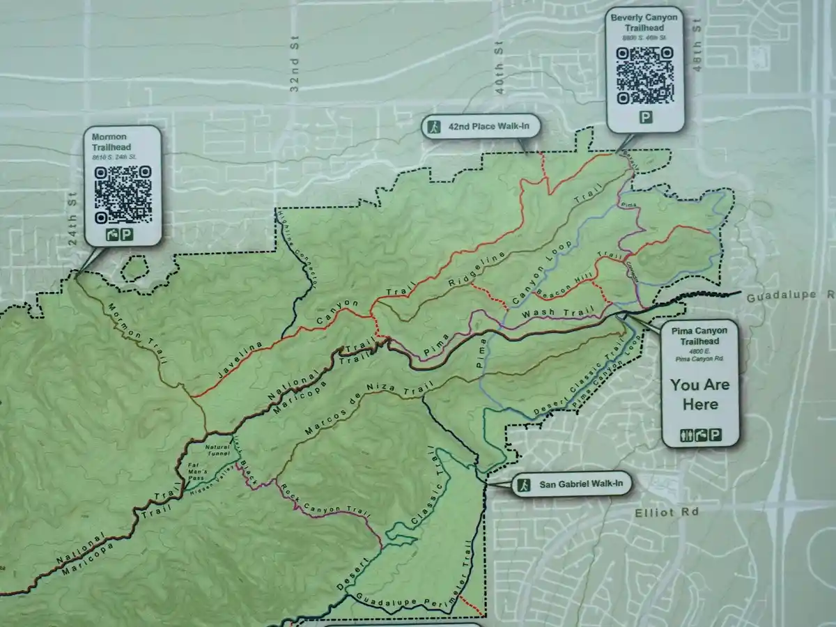 A trail map shows multiple hiking trails in a canyon area with labeled trailheads and QR codes. A white marker box near the…