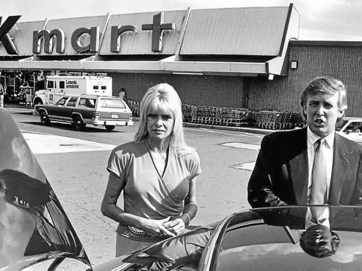 A black and white photo shows Donald Trump and Ivana Trump standing in a parking lot in front of a Kmart store. Trump is…