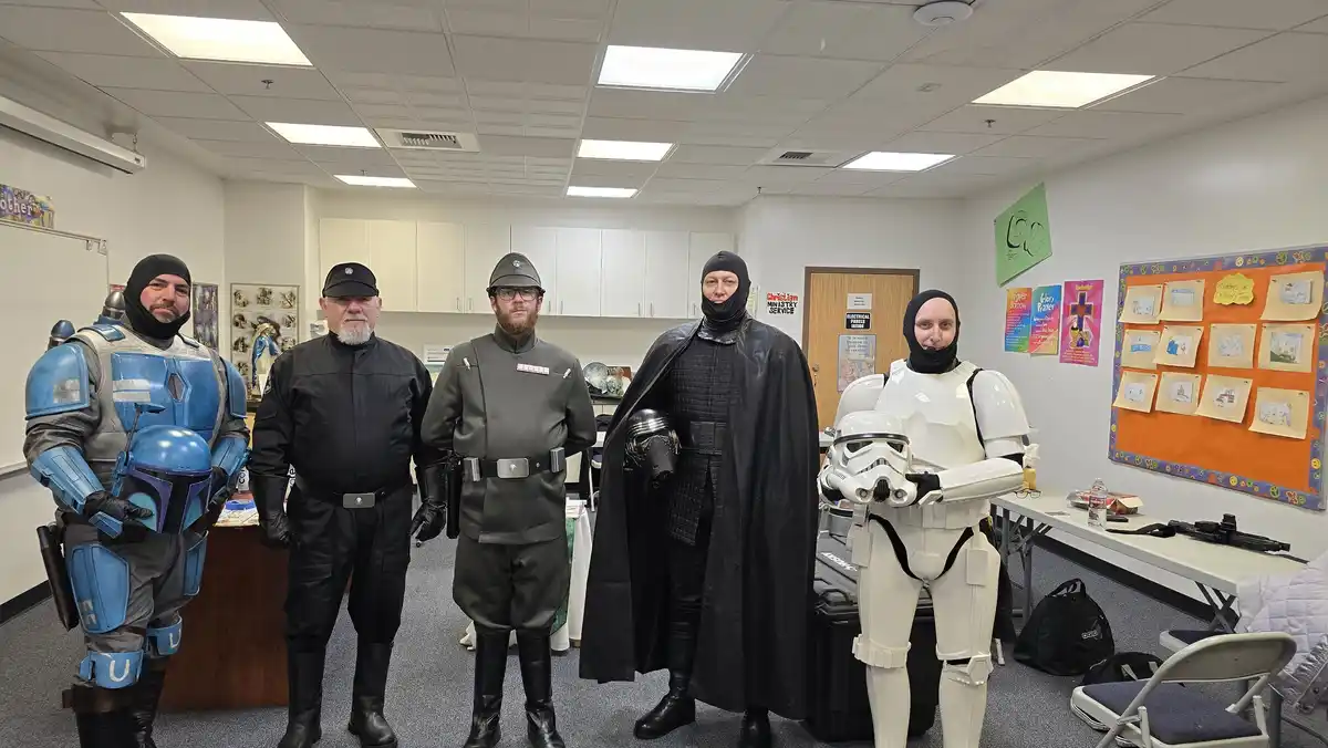Five men in Star Wars costumes — including a blue bounty hunter, a stormtrooper, and a dark-robed figure — stand in a church…