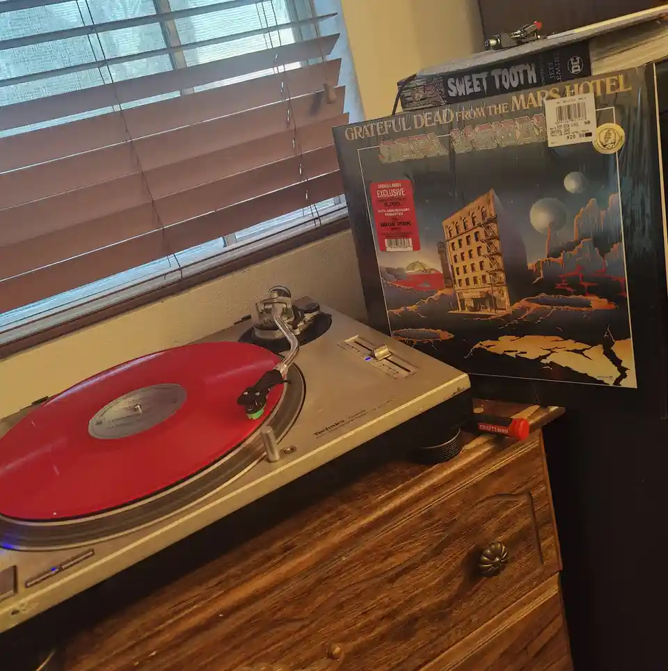 A Technics turntable plays a red vinyl record, with the album cover for 'Grateful Dead from the Mars Hotel' standing upright…