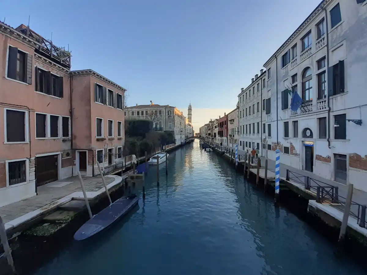 A scenic photo of a Venetian canal flanked by historic buildings under a clear blue sky, with a police station visible on…