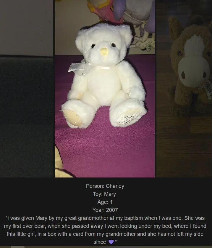 A white stuffed teddy bear named Mary sits on a purple fabric surface, with other stuffed animals partially visible in the…