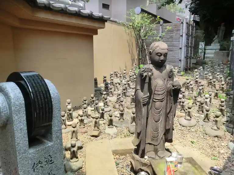 A large stone buddha statue stands in a courtyard surrounded by hundreds of smaller stone buddha statues. In the foreground…