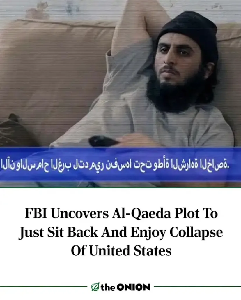 A man with a beard and black beanie lounges on a beige couch, one arm raised behind his head, holding a remote. A blue news…